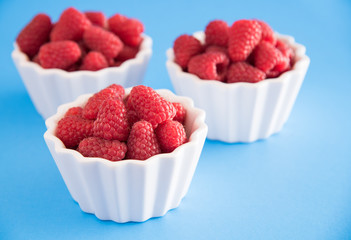 Fresh raspberries in three white bowls, on a blue background
