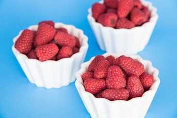 Fresh raspberries in three white bowls, on a blue background
