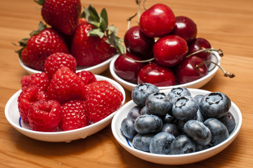 Small bowls of fruit containing cherries, strawberries, blueberries and rasberries on a wooden table