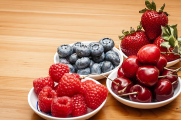 Small bowls of fruit containing cherries, strawberries, blueberries and rasberries on a wooden table