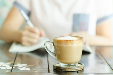 The cup of coffee on the table with working woman background in the coffee shop