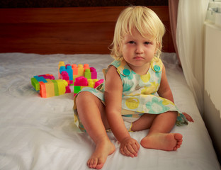 Fototapeta premium little blonde girl sits by window on sofa