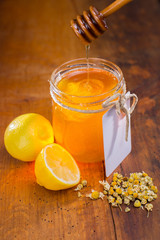 honey in a glass with label on a wooden table with chamomile tea and lemon