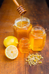 honey in a glass with label on a wooden table with chamomile tea and lemon
