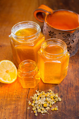 honey in a glass with label on a wooden table with chamomile tea and lemon

