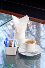 Espresso coffee with tissue paper, sac of sugar and creamer on mirror table.