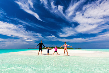 Happy family standing on the tropical beach holding hands