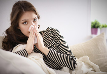 Portrait of a sick woman blowing her nose while sitting on the