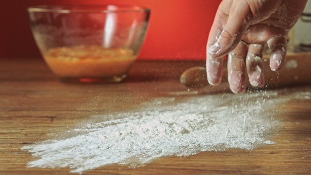 Baker hand throwing flour on the table, slow motion, 240 fps. Cooking and backing preparation. Food preparation on the red kitchen background.
