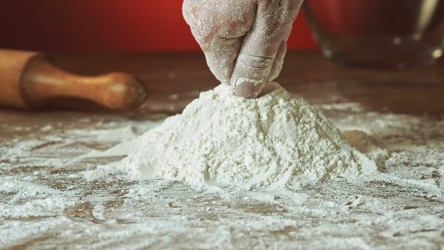 Baker hand preparing flour on the table to make dough, slow motion, 240 fps. Cooking and backing preparation. Food preparation on the red kitchen background.