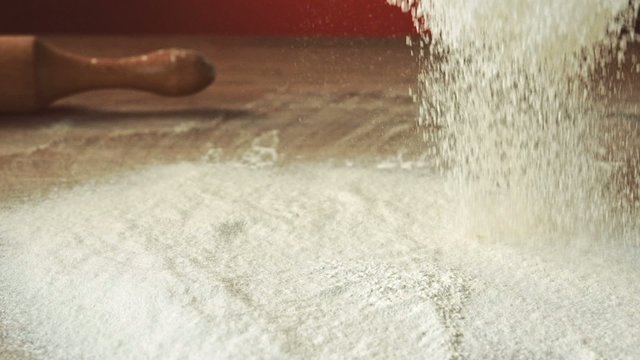 Sifting flour through sieve, slow motion 240fps. Baker sifting measured flour on a table. Cooking and backing preparation. Food preparation on the red kitchen background.
