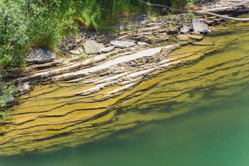 Bank of emerald mountain river consisting of layers of rock.