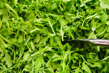 healthy arugula greens with serving tongs