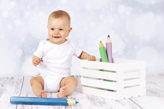 Little baby sitting on the floor with big coloring pencils