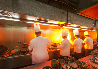 Chef in restaurant kitchen at stove with pan, doing flambe on food