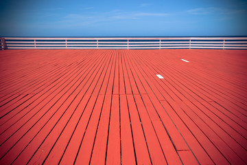 Red wood deck leading towards blue sky and ocean
