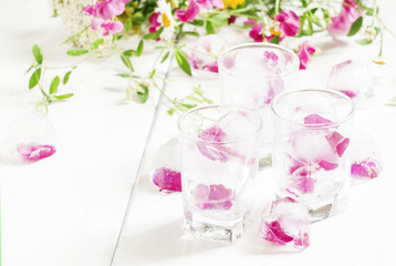 Ice cubes with rose petals on white wooden background, selective