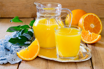Fototapeta na wymiar Orange juice in a glass and pitcher with mint, fresh fruits on wooden background