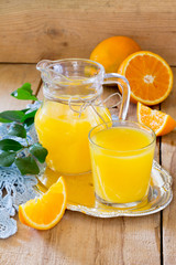 Orange juice in a glass and pitcher with mint, fresh fruits on wooden background