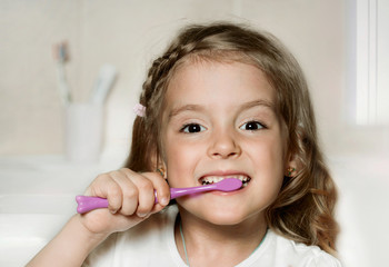 Child girl cleaning teeth with toothbrush in the bathroom.