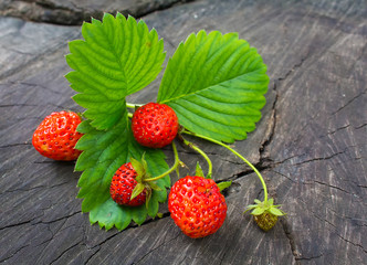 Ripe strawberries and green leaves on a wooden background