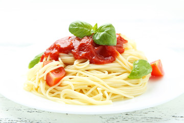 Spaghetti with tomatoes and basil on plate on white wooden backg