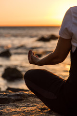 Silhouette young woman practicing yoga on the beach at sunset.