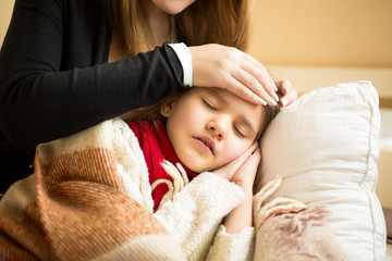 Closeup of caring mother holding head on sick daughter forehead