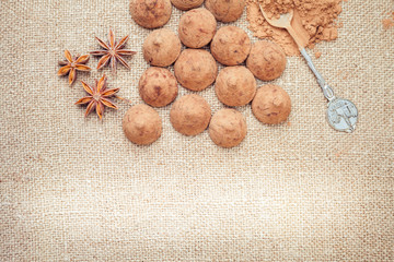 Chocolate truffles candies on a background of burlap bag texture with anise flowers, selective focus and vintage old style for chocolate day. There is a light spot for any text or design