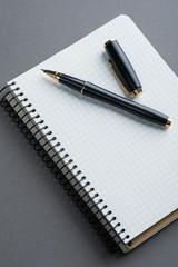 A spiral notebook with black ball pen over the grey background
