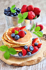 Pancakes with fresh strawberries, blueberries, maple syrup and honey, selective focus