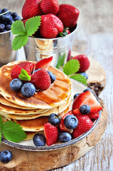 Pancakes with fresh strawberries, blueberries, maple syrup and honey, selective focus