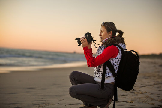 Girl photographer taking pictures with SLR camera at sunset on