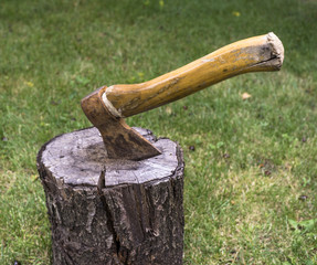 Ax driven into the wood timber in the yard on background of green grass