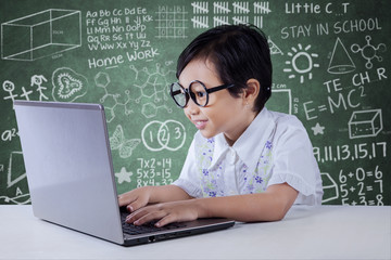 Modern little girl using laptop in classroom