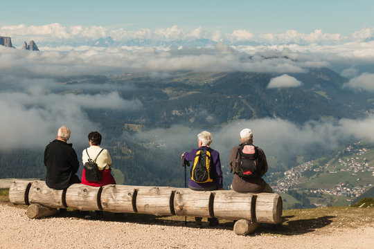 tourists resting on wooden bench above valley in Dolomites