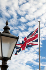 Union Jack flying with a cloudy sky as background and a lamppost as foreground 