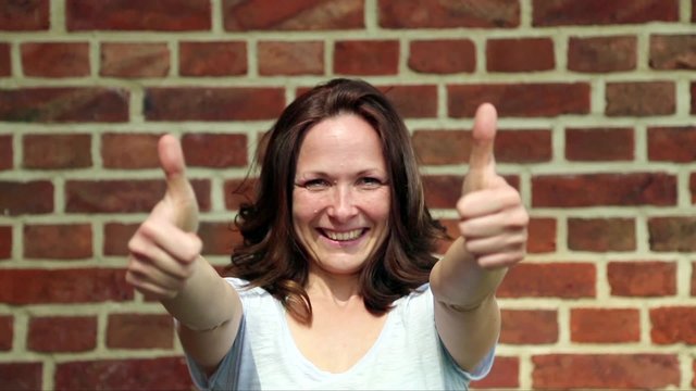 Frau zeigt zwei Daumen hoch, im Hintergrund ist eine Backsteinwand