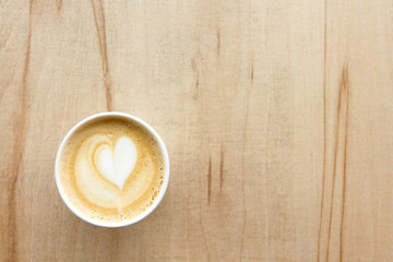 Cappuccino with heart in paper take away cup on light wood table