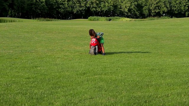 Cute afro boy plays and drives with the red motorbike toy on the sunny glade.