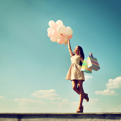 Beautiful girl holding shopping bags and colored ballons over bl