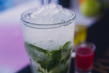 Beautiful line of different colored alcohol mojito cocktails with mint on a open air party, tequila, martini, vodka, and others on decorated catering bouquet table on open air event party.