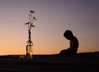 silhouette of a lonely boy with a bouquet of daisies at sunset