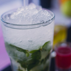 Beautiful line of different colored alcohol mojito cocktails with mint on a open air party, tequila, martini, vodka, and others on decorated catering bouquet table on open air event party.