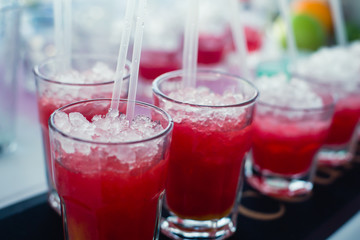Beautiful line of different colored alcohol mojito cocktails with mint on a open air party, tequila, martini, vodka, and others on decorated catering bouquet table on open air event party.