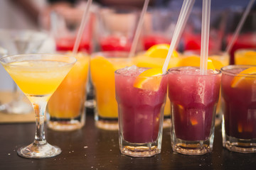 Beautiful line of different colored alcohol mojito cocktails with mint on a open air party, tequila, martini, vodka, and others on decorated catering bouquet table on open air event party.