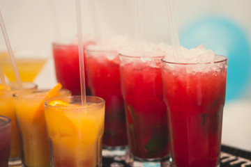 Beautiful line of different colored alcohol mojito cocktails with mint on a open air party, tequila, martini, vodka, and others on decorated catering bouquet table on open air event party.
