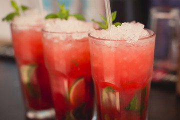 Beautiful line of different colored alcohol mojito cocktails with mint on a open air party, tequila, martini, vodka, and others on decorated catering bouquet table on open air event party.