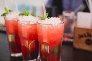 Beautiful line of different colored alcohol mojito cocktails with mint on a open air party, tequila, martini, vodka, and others on decorated catering bouquet table on open air event party.