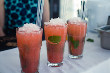 Beautiful line of different colored alcohol mojito cocktails with mint on a open air party, tequila, martini, vodka, and others on decorated catering bouquet table on open air event party.